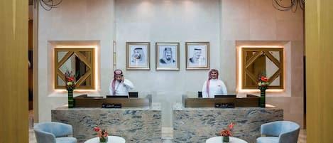 A reception area with two receptionists, marble counters, framed portraits, and seating with vases.
