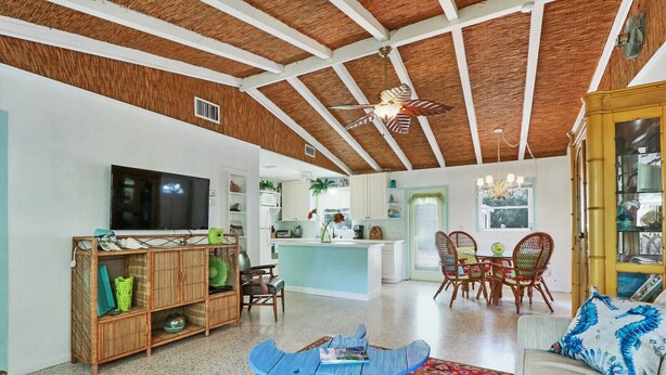 A spacious living area with a high ceiling, a TV, a dining table with chairs, a kitchen area, and a small island. - Old Florida Surf Cottage (Jensen Beach)