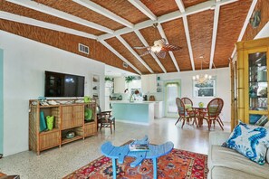 A spacious living area with a high ceiling, a TV, a dining table with chairs, a kitchen area, and a small island. - Old Florida Surf Cottage (Jensen Beach)