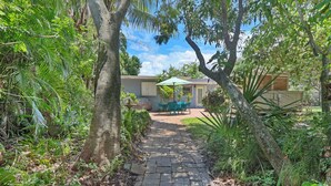 A pathway leading to a house with a patio area, surrounded by lush greenery and trees. - Old Florida Surf Cottage (Jensen Beach)
