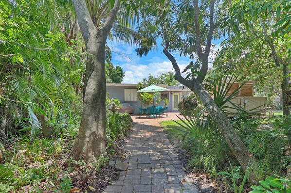 A pathway leading to a house with a patio area, surrounded by lush greenery and trees. - Old Florida Surf Cottage (Jensen Beach)