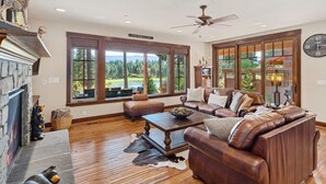 A spacious living room with a fireplace, leather sofas, a coffee table, and large windows offering a view of the outdoors. - Golf View, Hot Tub, Suncadia Pool Access (Cle Elum)