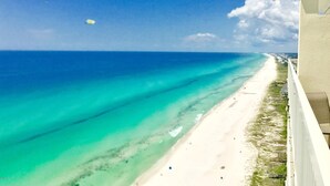 Vista de una playa con aguas turquesas cristalinas, una orilla arenosa y un edificio blanco con balcón.