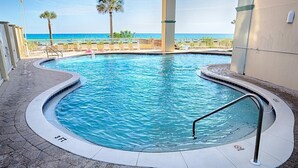 Una piscina con indicador de profundidad de 3 pies, rodeada por un deck de baldosas y palmeras, con vista a una playa.