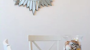 Una mesa de comedor con un espejo radiante en la parte superior, un florero de vidrio con caracolas y una silla blanca.