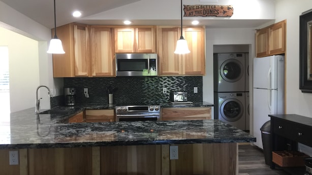 A modern kitchen with wooden cabinets, a granite countertop, stainless steel appliances, and a sign above the sink. - Direct Dune Access Sleeps 10 In House, 6 In BunkHouses - Bath Houses. (North Bend)