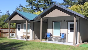 A two-story building with a covered porch, a small table, and two folding chairs. - Direct Dune Access Sleeps 10 In House, 6 In BunkHouses - Bath Houses. (North Bend)