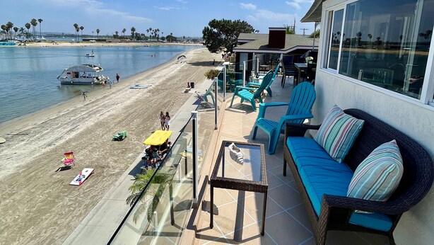 A balcony with a view of a beach and the ocean. There are blue chairs and a table on the balcony. - The BEST of the best on Mission Bay! (San Diego)
