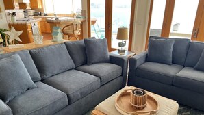 A living room with two grey sofas, a wooden coffee table with a tray, and a view of the kitchen and balcony. - The BEST of the best on Mission Bay! (San Diego)