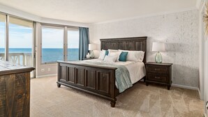Een slaapkamer met een groot bed, een nachtkastje en een dressoir. Er is uitzicht op de oceaan door het raam.