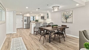 Een moderne keuken met witte kastjes, een centraal eiland en een eetgedeelte met een houten tafel en stoelen.