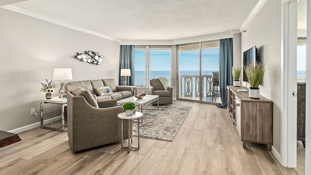 Een moderne woonkamer met een bank, salontafel en televisie. Er is een balkon met uitzicht op de oceaan.