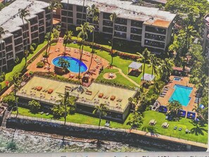 An aerial view of a hotel with a central pool, multiple guest rooms, and a beachfront.