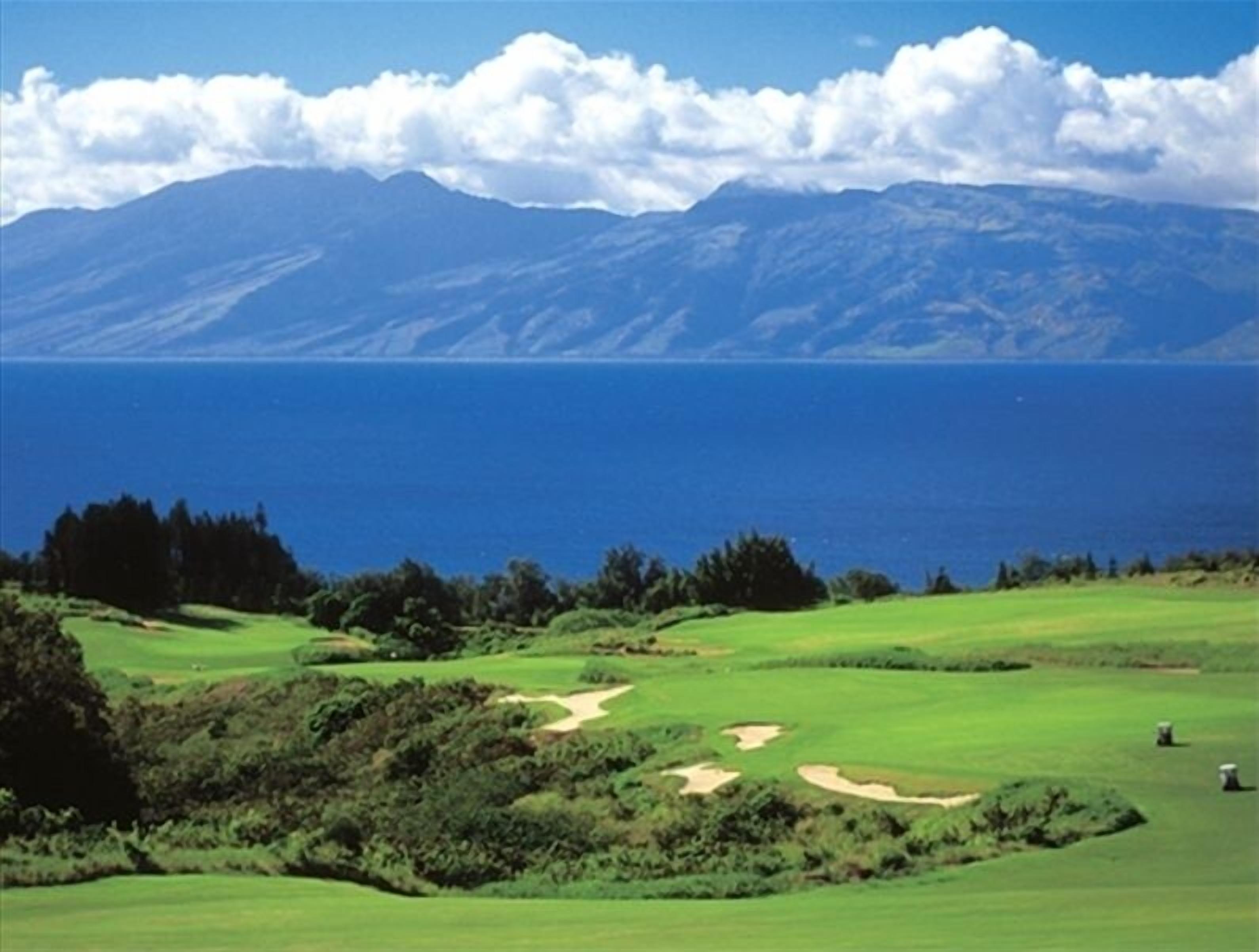Een golfbaan met uitzicht op de oceaan en bergen op de achtergrond.