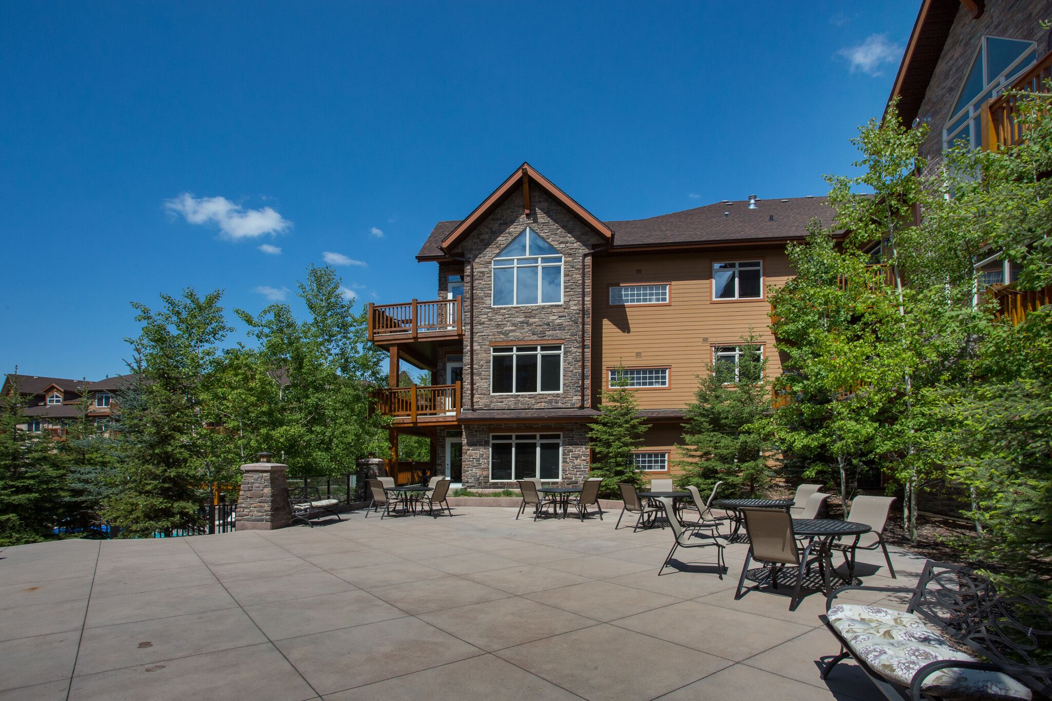 A multi-story building with a stone facade, a balcony on the second floor, and outdoor seating area with tables and chairs.