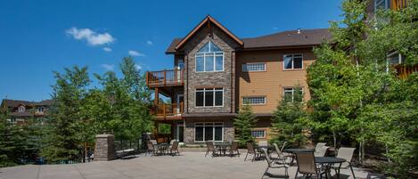 A multi-story building with a stone facade, a balcony on the second floor, and outdoor seating area with tables and chairs.