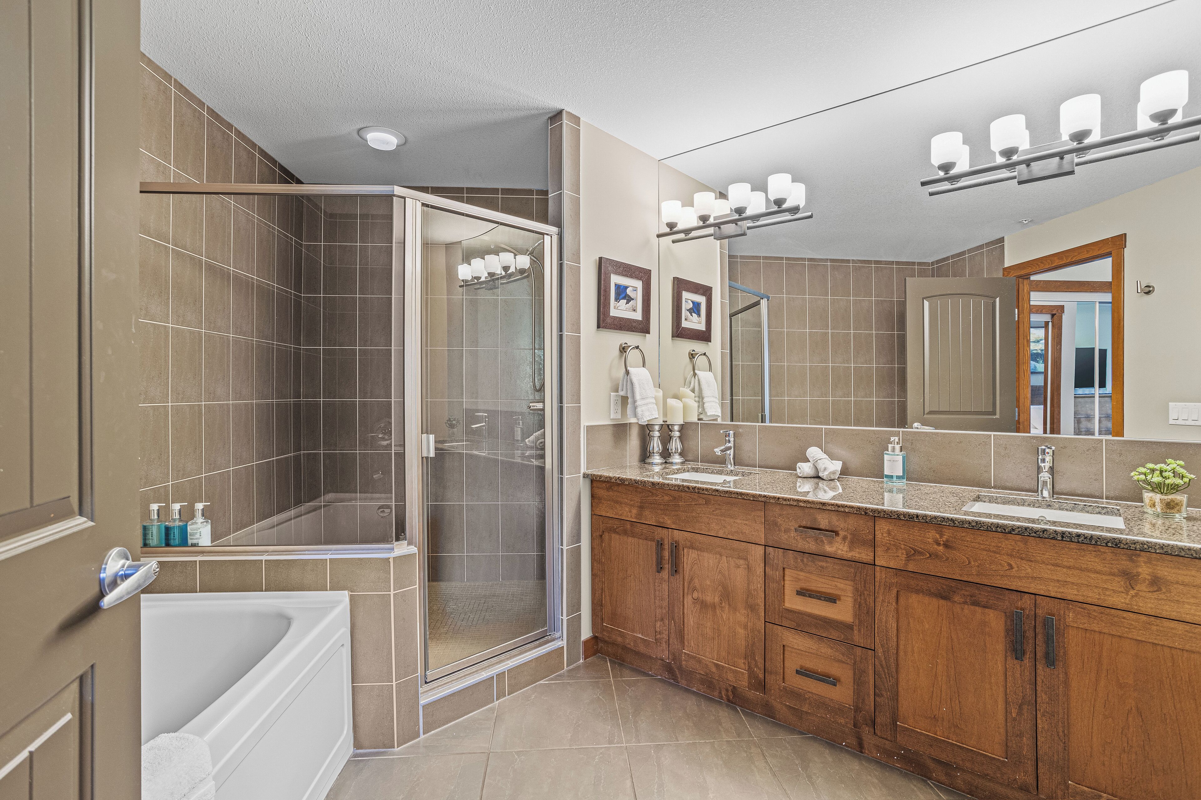 A modern bathroom with a walk-in shower, a bathtub, and a vanity with a large mirror and multiple lights.