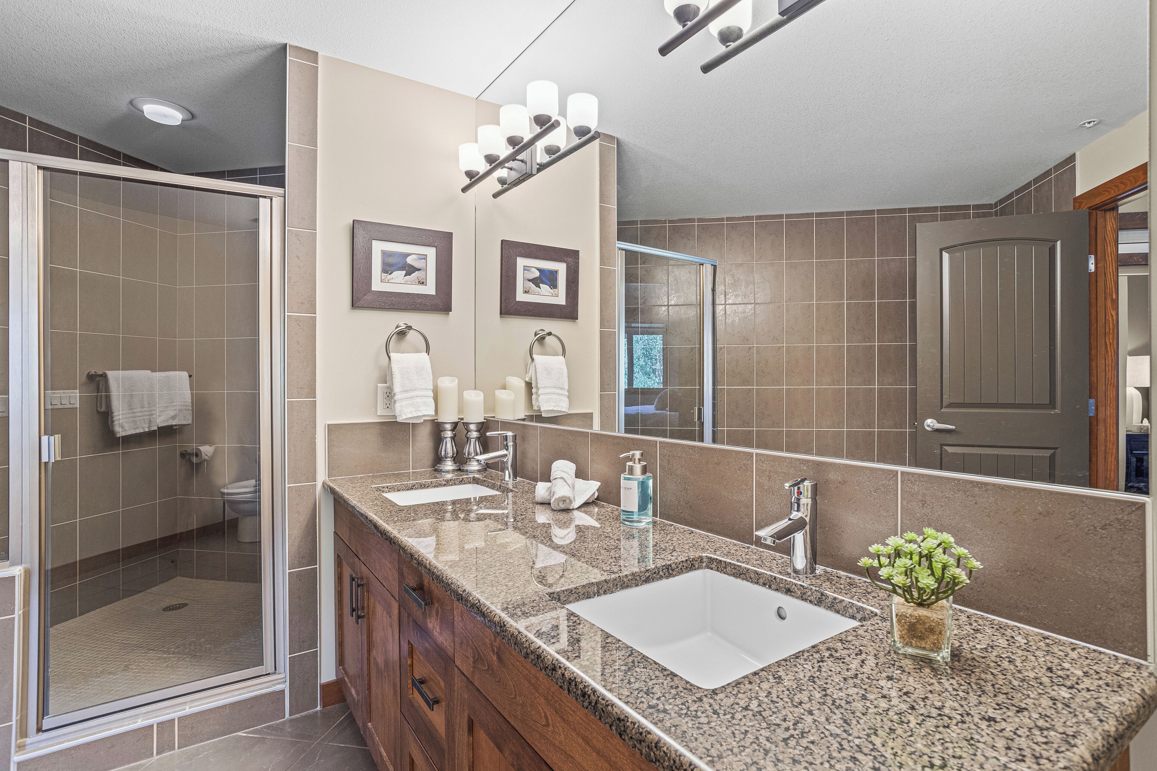 A modern bathroom with a large mirror, two sinks, a shower, and a vanity with cabinets.