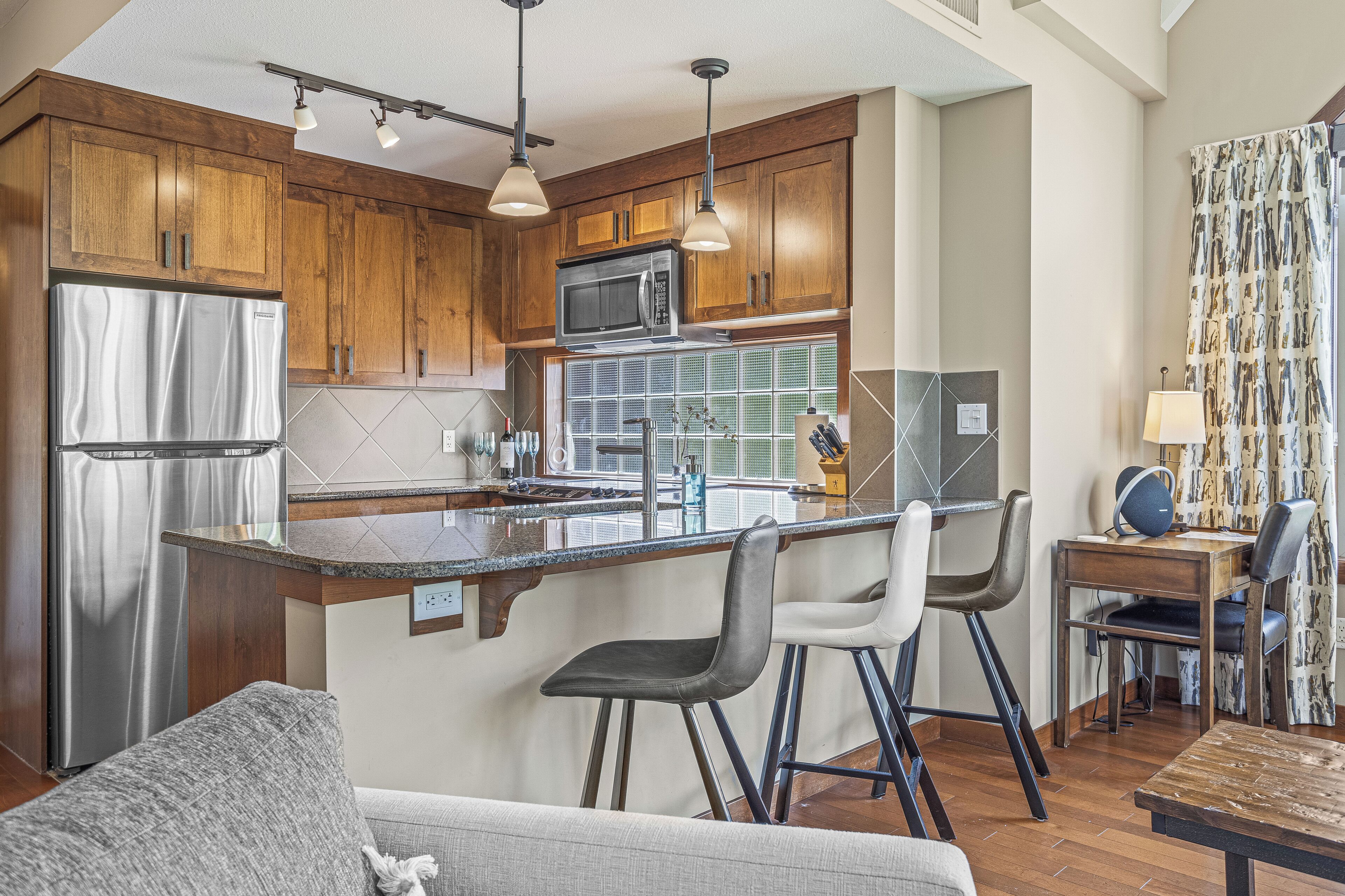 A kitchen with wooden cabinets, stainless steel appliances, a central island with bar stools, and a dining area with a table and chairs.