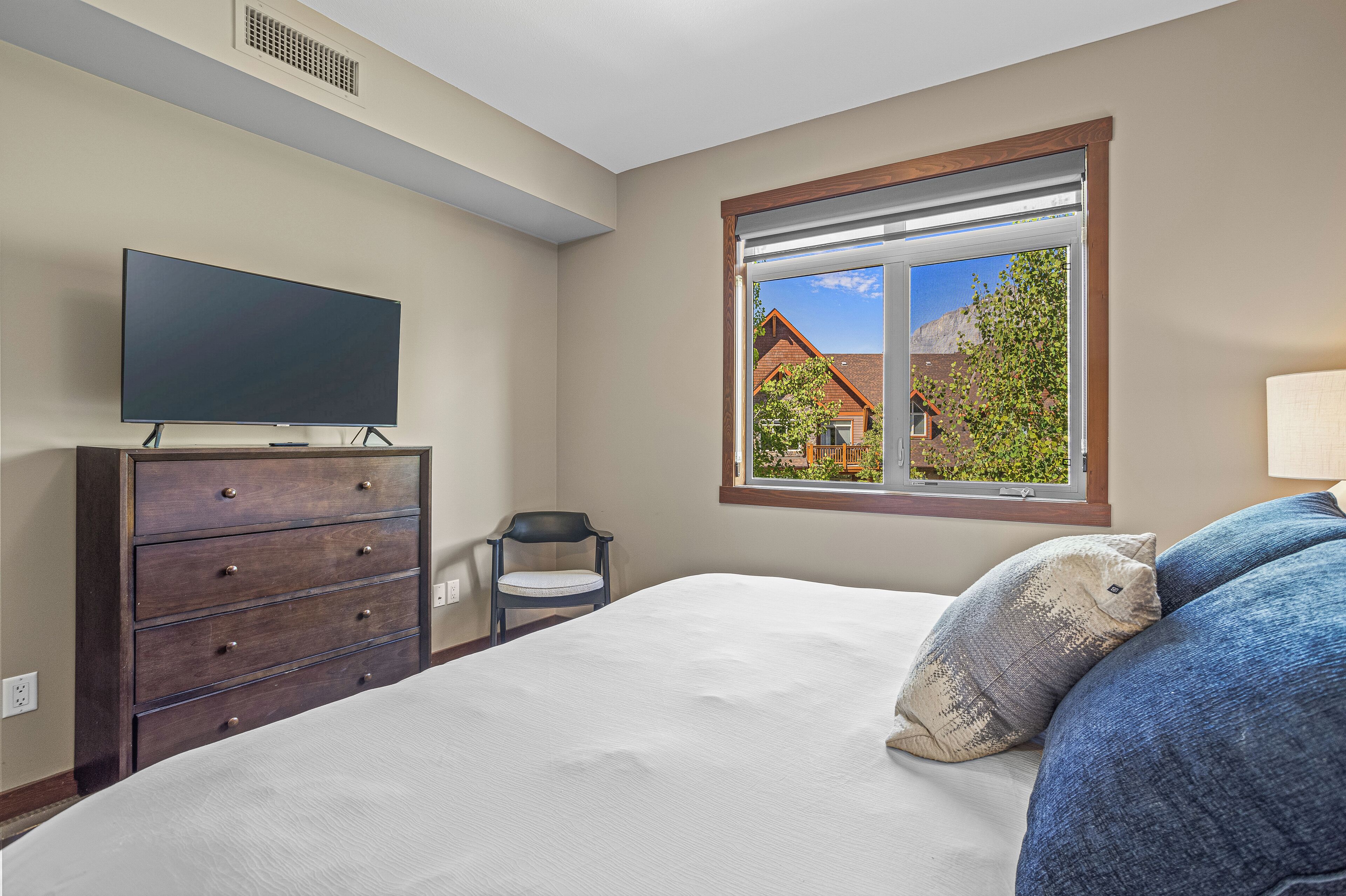 Een slaapkamer met een bed, een dressoir, een stoel en een televisie.