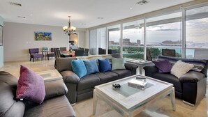 A spacious living room with a large window, a sofa set, a coffee table, and a dining area. - Luxurious 4 Bed/4 Bath with Million Dollar Views (Cozumel Island)