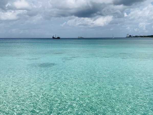 Une mer turquoise aux eaux limpides, parsemée de bateaux, avec une côte qui se dessine à l’horizon.