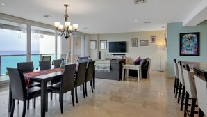 A dining area with a view of the sea, a TV, and a painting on the wall. - Luxurious 4 Bed/4 Bath with Million Dollar Views (Cozumel Island)