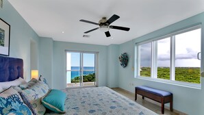 A bedroom with a large bed, a ceiling fan, a bench, and a view of the ocean through large windows. - Luxurious 4 Bed/4 Bath with Million Dollar Views (Cozumel Island)