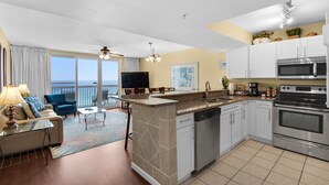 A kitchen with a dishwasher, oven, and microwave. There is a dining area with a table and chairs, and a balcony with a view. - 1BR/2BA,Gorgeous 10th Floor Oceanfront,  Awesome View! (Destin)