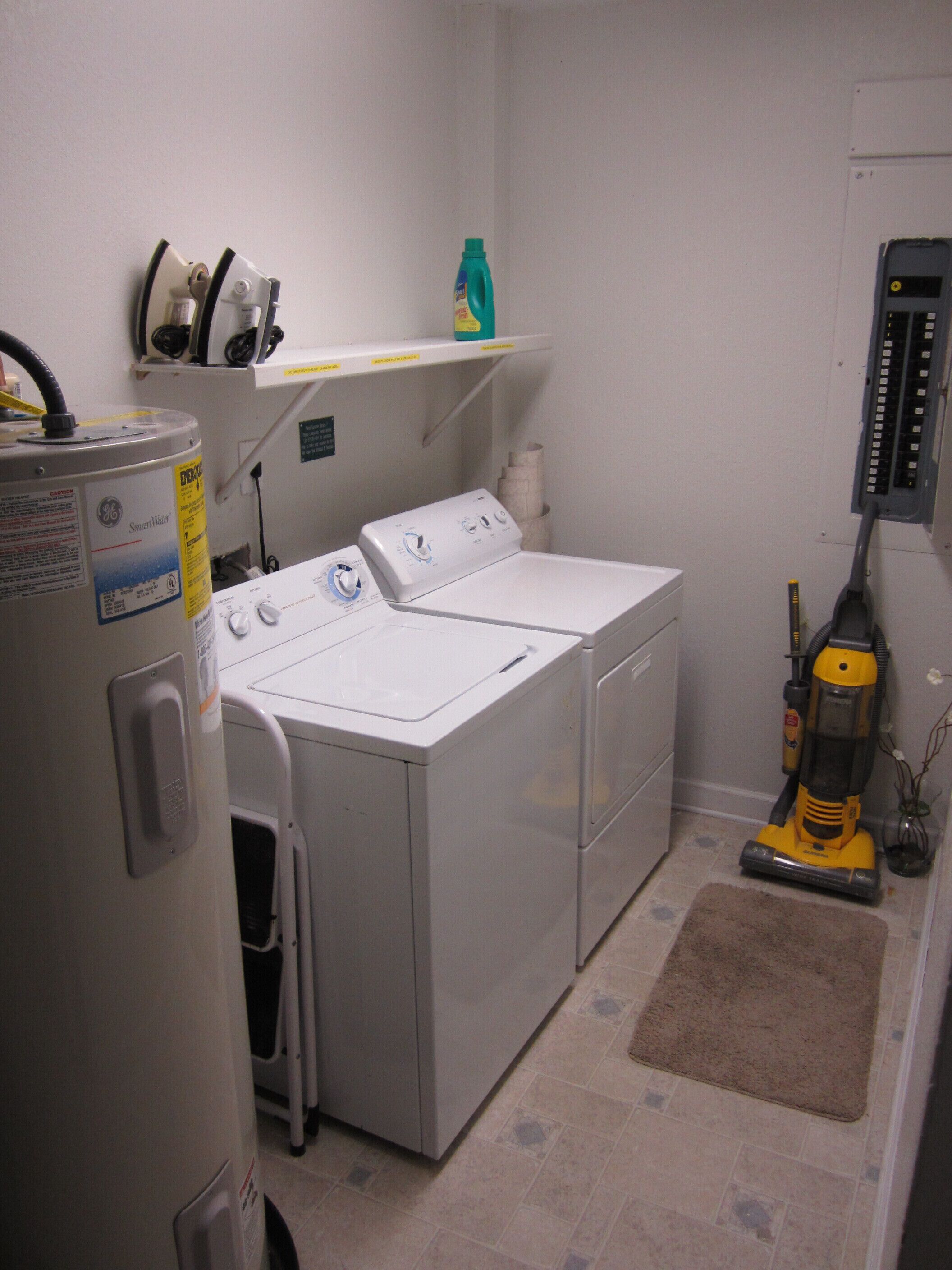 A laundry room with a front-loading washer and dryer, a vacuum cleaner, and a water heater.