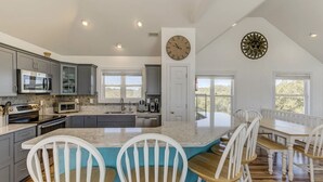 A spacious kitchen with grey cabinets, a large island with chairs, and a clock on the wall. - A Beach Vacation destination. EV friendly. (Corolla)