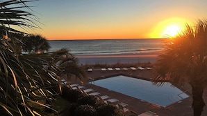 Une piscine bordée de chaises longues, de palmiers et offrant une vue imprenable sur le coucher de soleil.