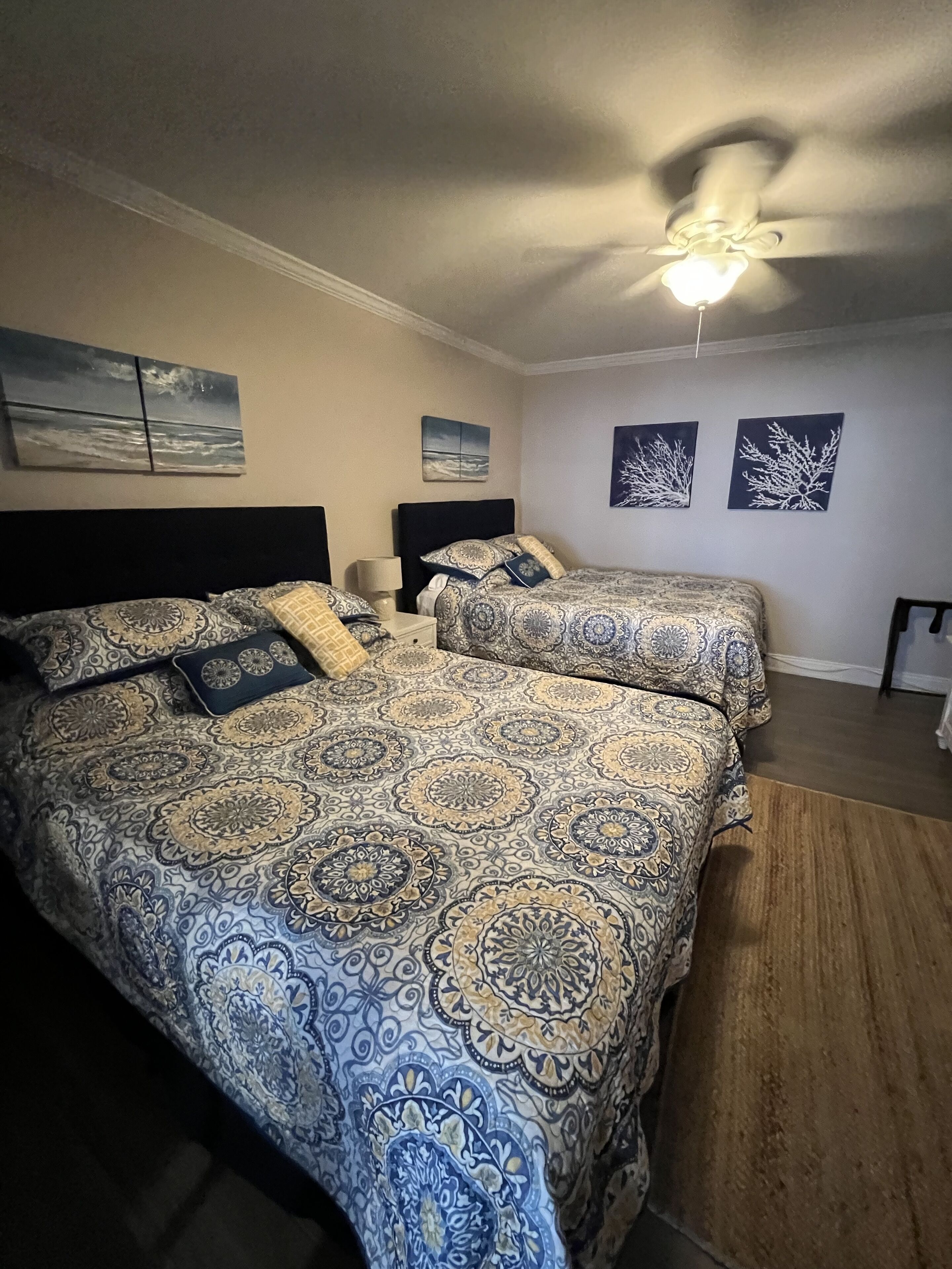 A bedroom with two beds, a ceiling fan, and artwork on the walls.