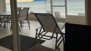 Une pièce dotée de grandes fenêtres donnant sur la mer, avec un parasol bleu et un ventilateur de plafond.