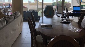 Un coin repas avec vue sur la plage, un ventilateur de plafond et un ordinateur portable posé sur un bureau.