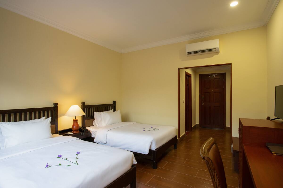 Une chambre d’hôtel avec deux lits, un bureau, une chaise, une lampe et un appareil de climatisation.