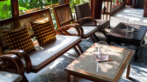 A sunlit outdoor seating area with wooden furniture and a glass table.