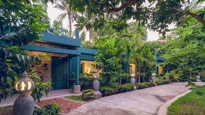 A pathway leading to a building with a blue facade, surrounded by lush greenery and decorative urns.
