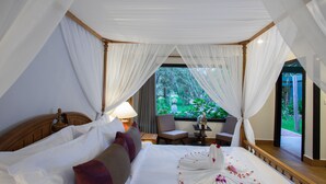 A spacious bedroom with a large bed, a sitting area with a chair and table, and a view of greenery outside.