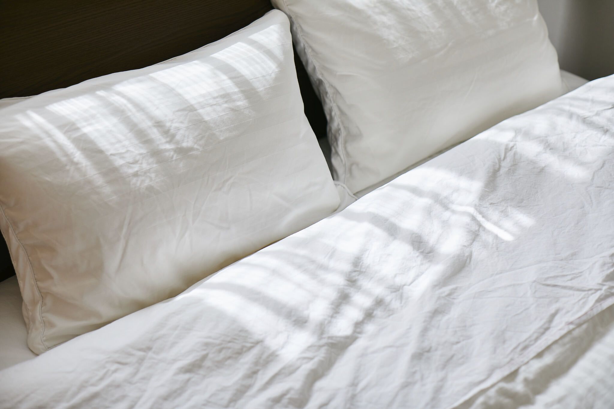A bed with white linens and pillows.