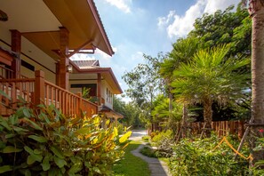 A pathway leading to a wooden building with a balcony, surrounded by lush greenery and palm trees. - Baan Pondchanok Hotel (Hang Dong)