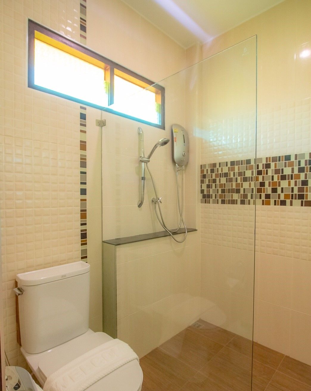 A bathroom with a toilet, a shower with a glass door, and a tiled wall with a mosaic pattern.