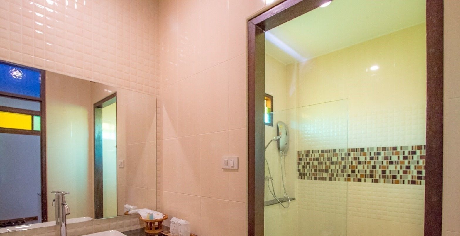 Een badkamer met een glazen douchecabine, een wastafel met spiegel en een betegelde muur met mozaïekpatroon.