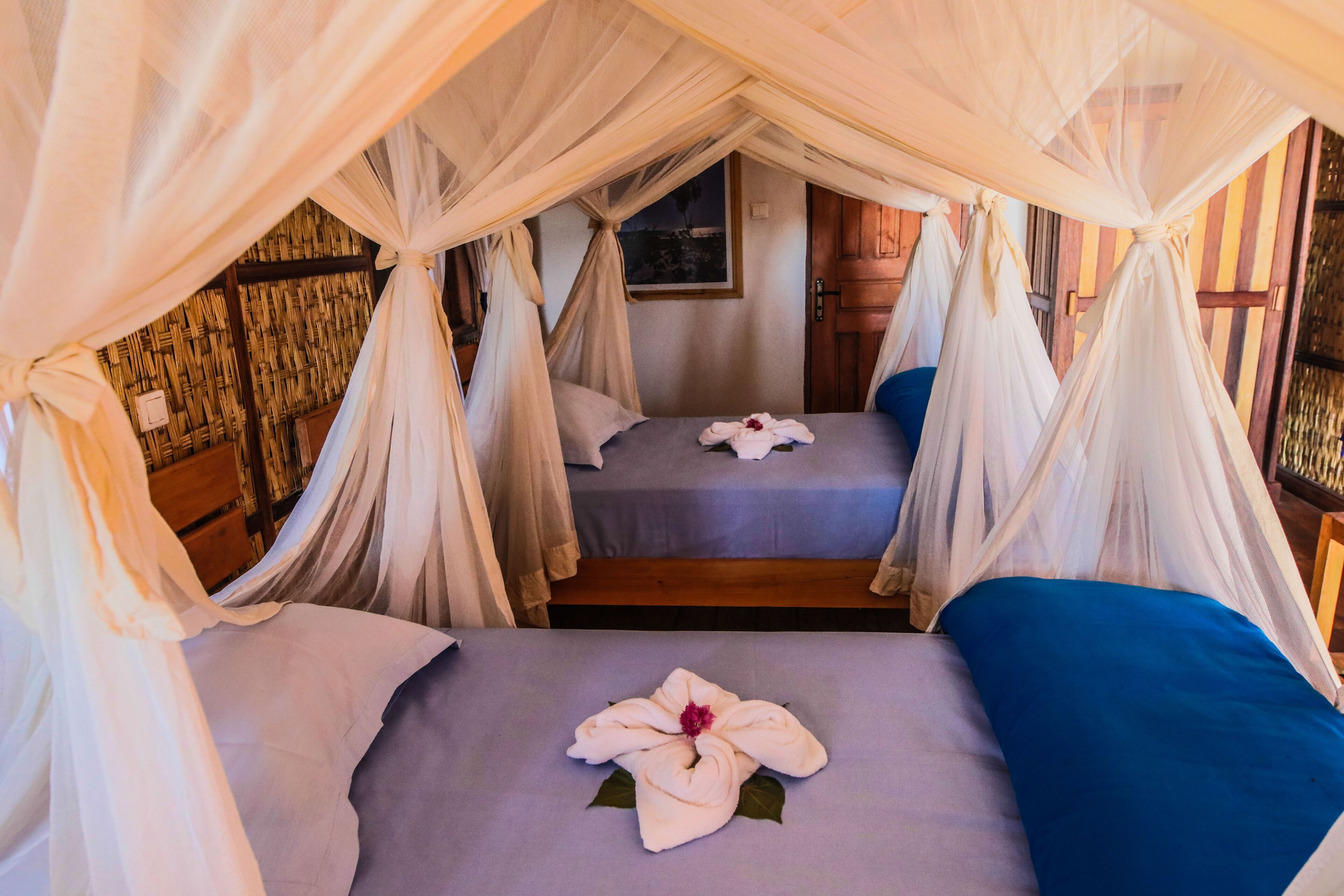 A room with two beds, each with a canopy and a flower arrangement on the bed.