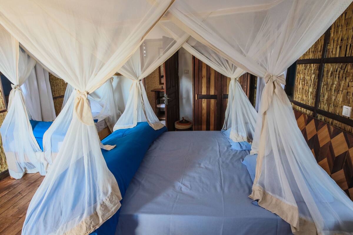 A room with a bed covered by a canopy, a blue sofa, and a wooden wall.