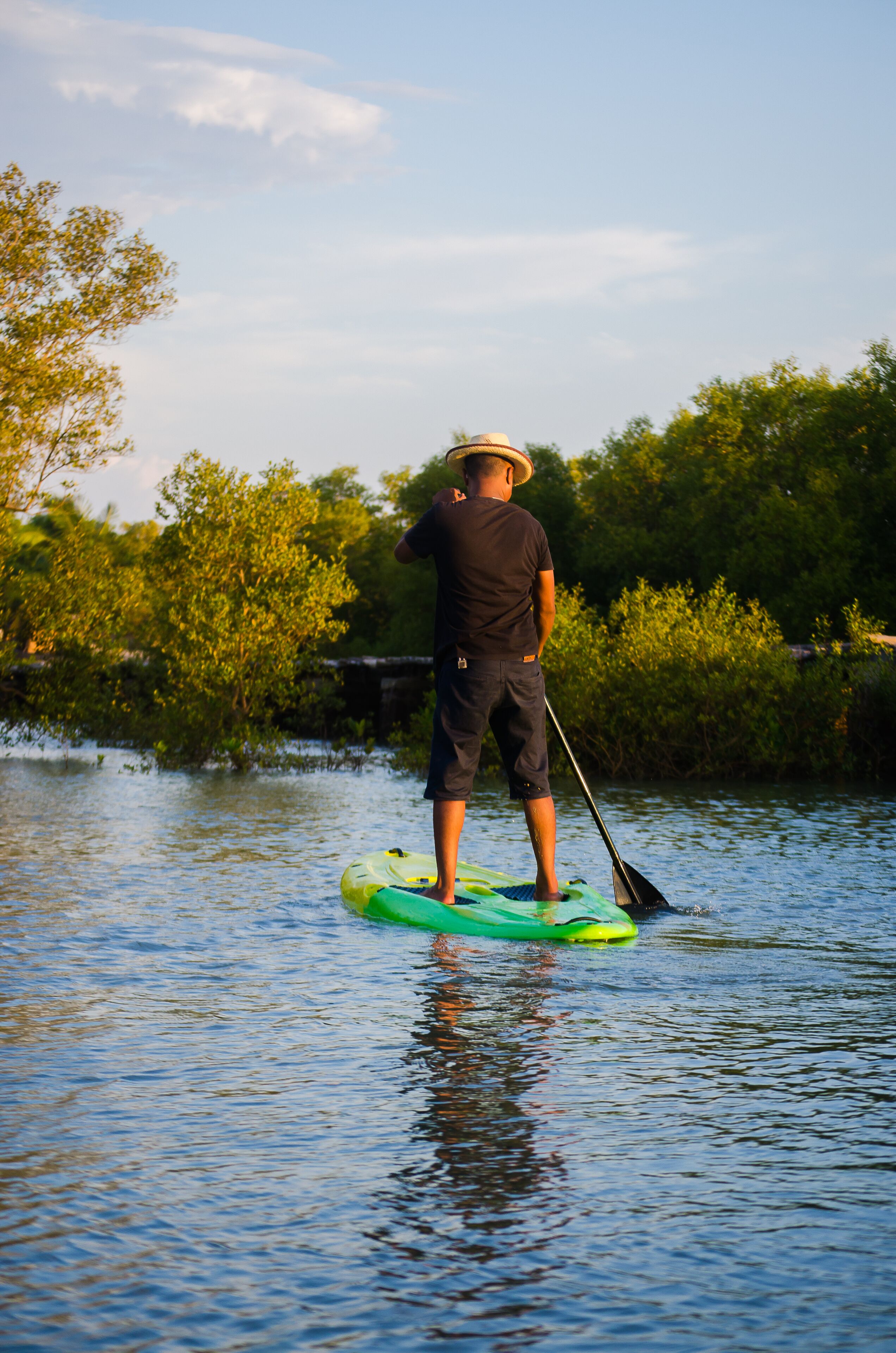 Eine Person steht auf einem grünen Stand-Up-Paddle auf einem Gewässer, umgeben von viel Grün.