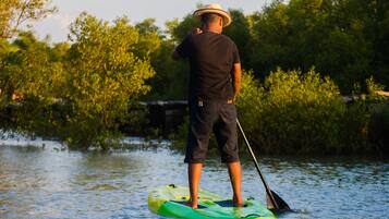 Eine Person steht auf einem grünen Stand-Up-Paddle auf einem Gewässer, umgeben von viel Grün.