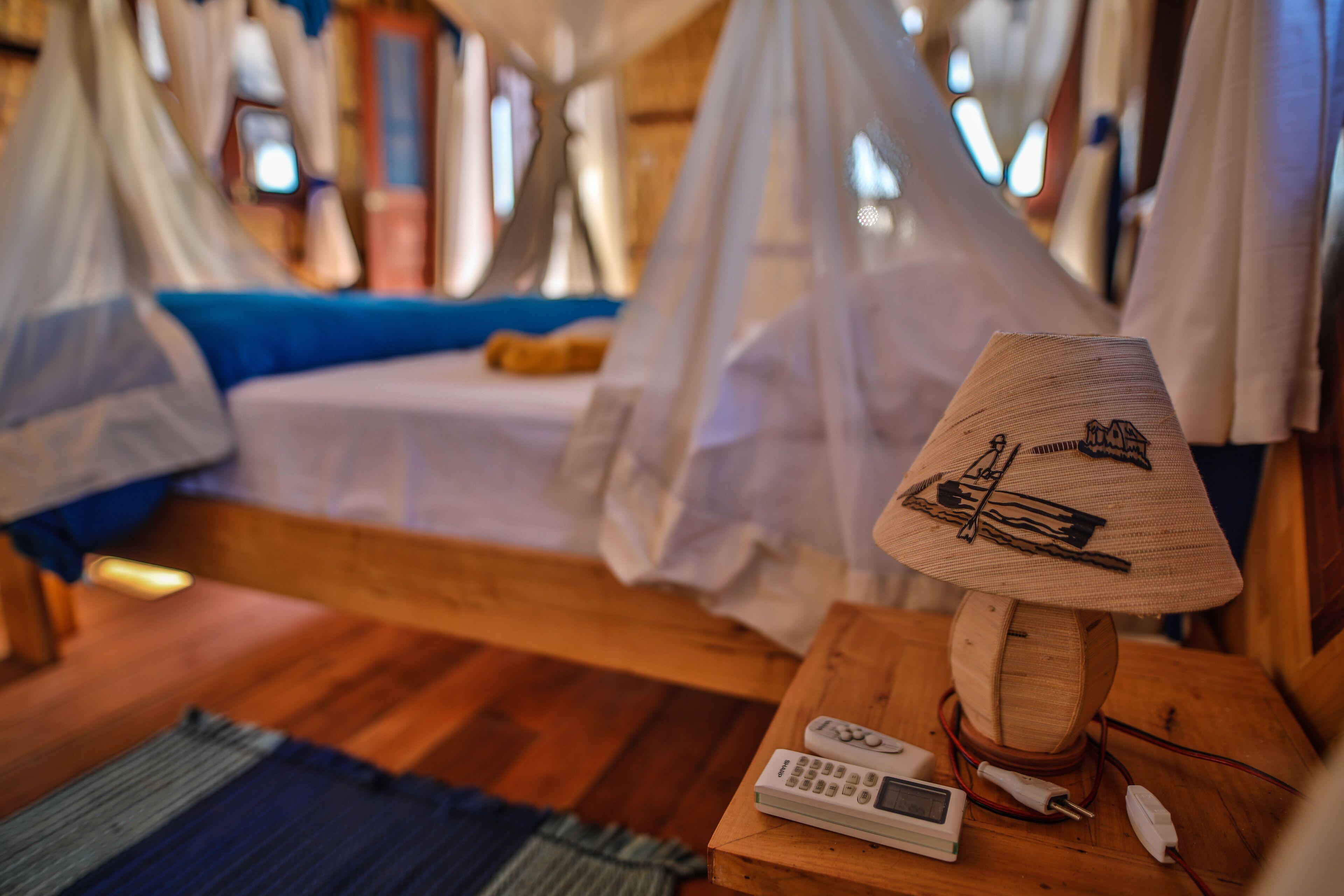 A room with a bed, a wooden nightstand with a lamp, and a small table with a remote control and a power strip.
