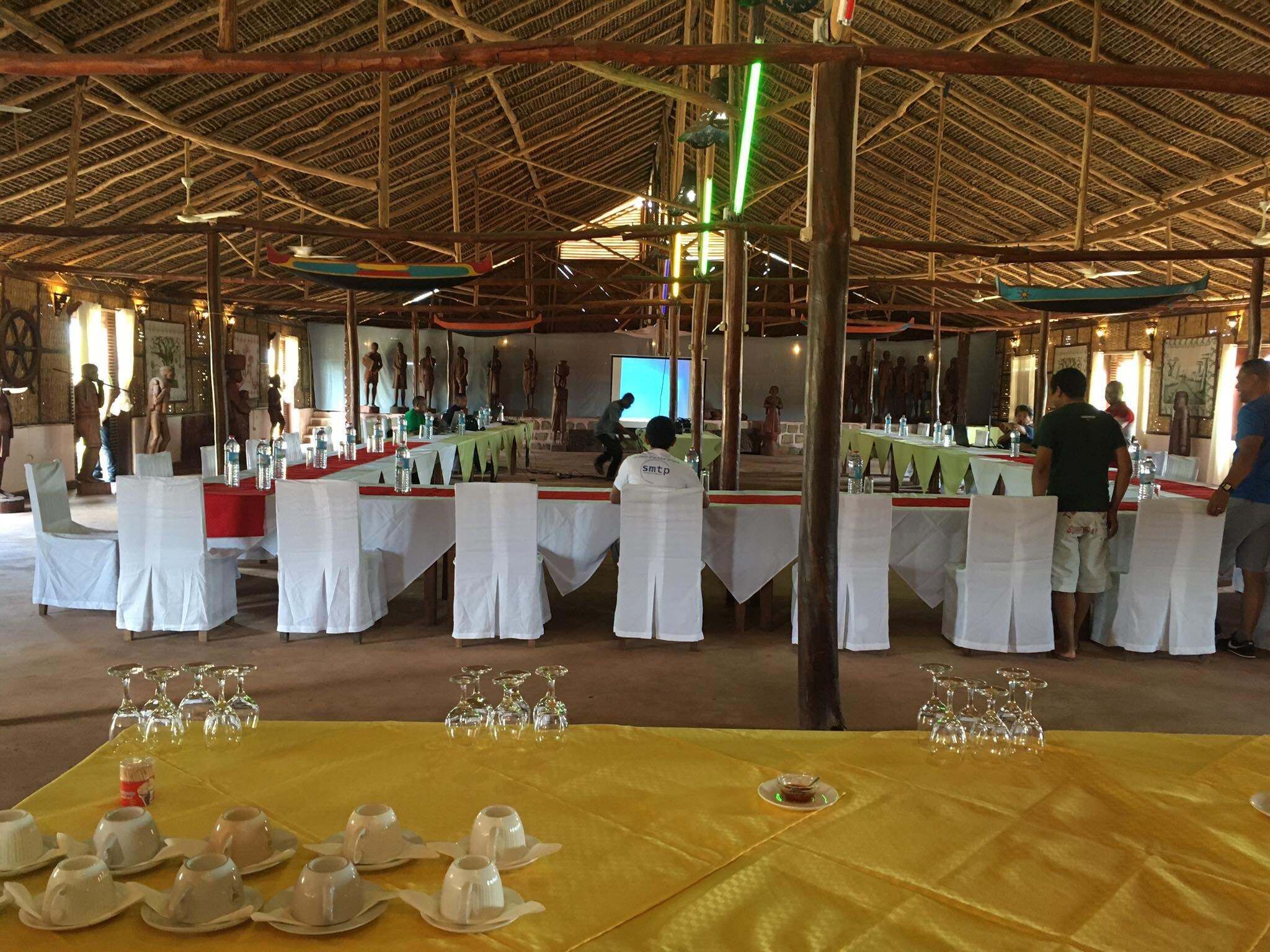 A banquet hall with multiple round tables covered with white tablecloths, arranged in rows.