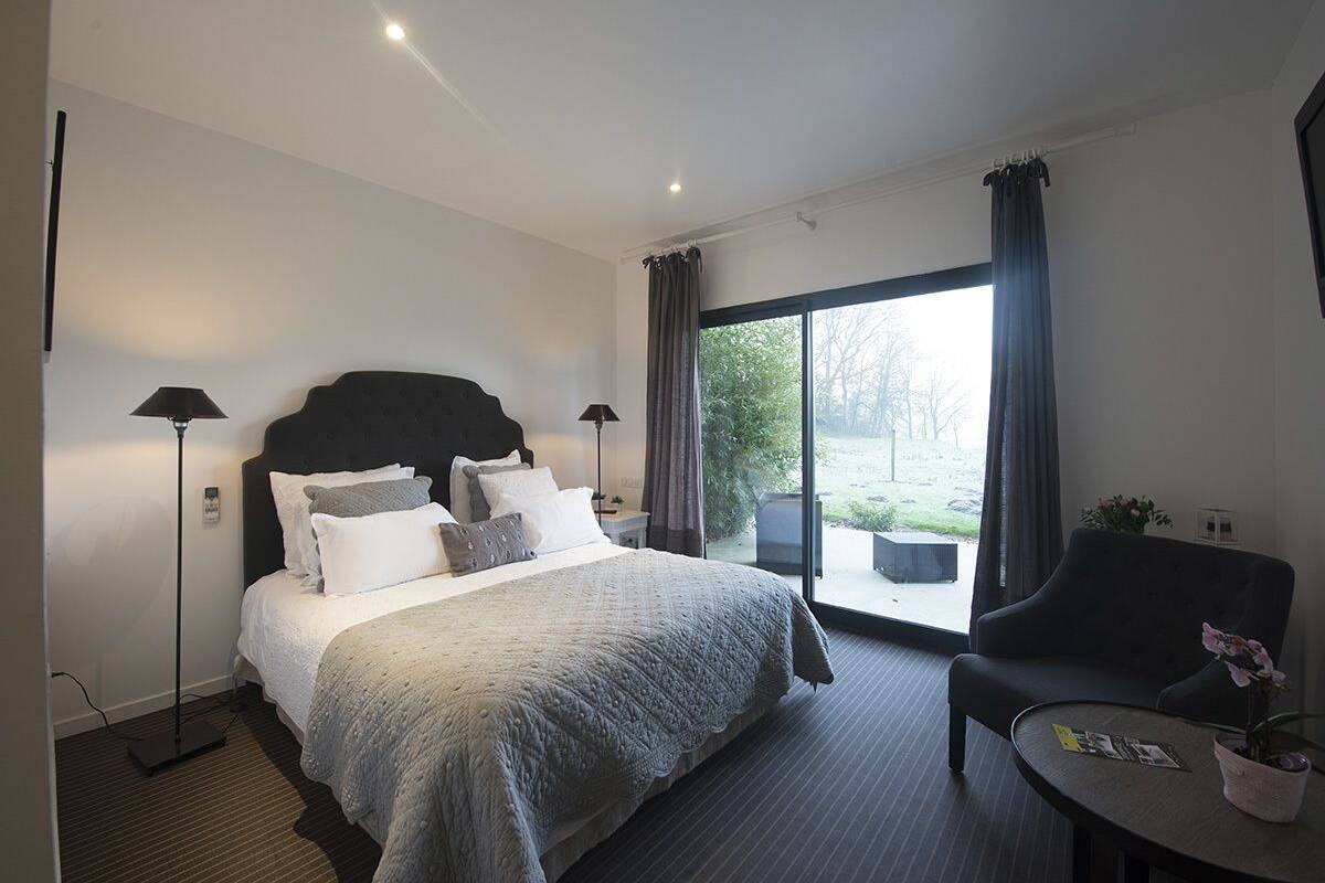Een moderne hotelkamer met een groot bed, een bureau, een stoel en uitzicht op het omliggende landschap.